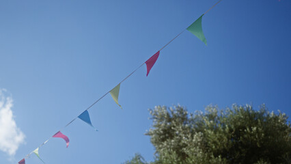 Colorful flags flying against a clear blue sky with trees in the background in mallorcan outdoors, spain.