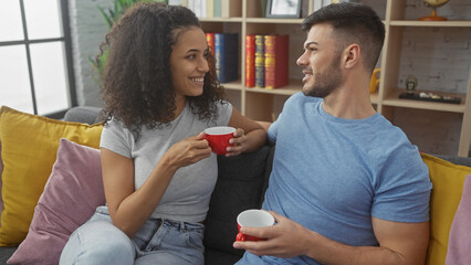 A smiling woman and man holding red cups while sitting comfortably on a sofa in a cozy living room.