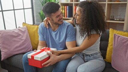 A man and woman lovingly exchange a gift on a cozy sofa in a modern living room, evoking feelings of romance and togetherness.