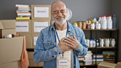 Smiling bearded man with a volunteer badge standing in a donation center full of boxes and supplies.