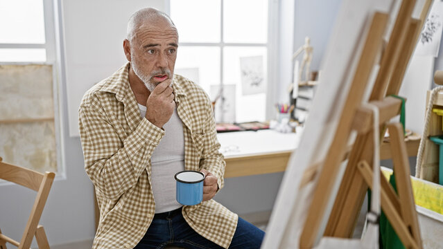 Pensive man with grey beard holding mug in art studio - Powered by Adobe