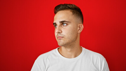 Handsome young adult hispanic man isolated against a red wall background, looking to the side, thoughtful expression