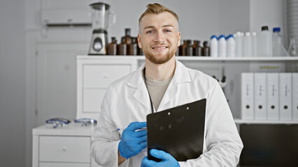 Confident young man with beard in lab coat holding clipboard in a modern laboratory