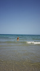 Obraz premium Woman enjoying the ocean waters in a sunny outdoor setting with a clear blue sky and gentle waves along a sandy beach