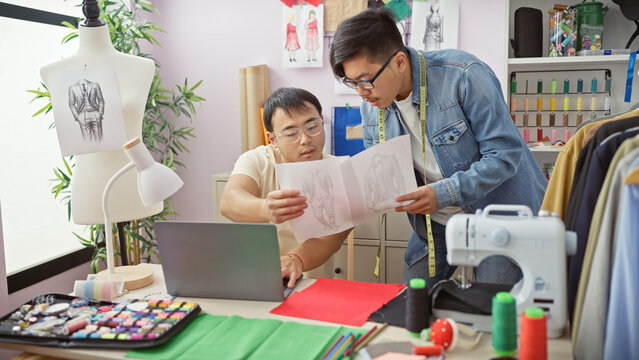 Two men review a garment design in a bright tailor shop filled with sewing equipment and fabric samples.