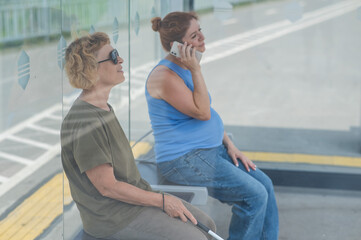 Fototapeta premium An elderly blind woman and a pregnant woman are sitting at a bus stop and waiting for the bus.