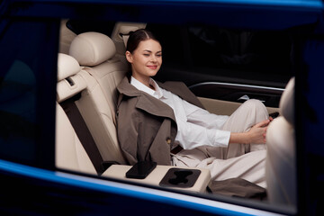 Woman in back seat of car with hand on front seat arm rest, displaying a relaxed and comfortable...