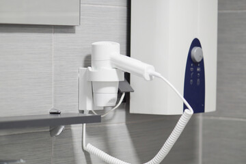 White electric hairdryer on a wall next to a mirror. Bathroom