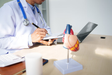 A medical doctor is working at a desk, analyzing patient data related to heart attacks and calculating medical costs to ensure accurate billing and financial management in the healthcare setting.