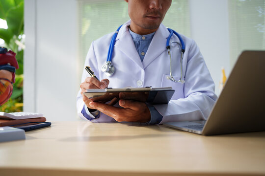 A medical doctor is working at a desk, analyzing patient data related to heart attacks and calculating medical costs to ensure accurate billing and financial management in the healthcare setting.