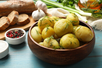 Tasty young boiled potatoes with dill in bowl on light blue wooden table
