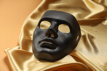 Theater arts. Black mask and golden fabric on pale orange background, closeup