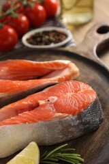 Board with fresh salmon steaks, lemon and rosemary on table, closeup