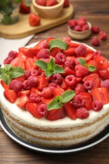 Tasty sponge cake with fresh berries and mint on wooden table, closeup