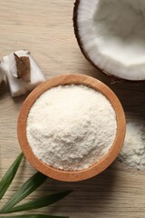 Fresh coconut flour in bowl, nut and palm leaf on wooden table, flat lay