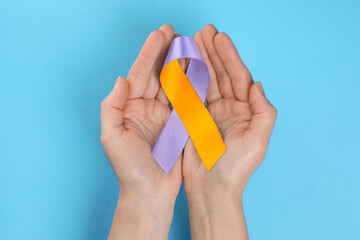 World Psoriasis Day. Woman with orange and orchid ribbon as symbol of support on light blue background, top view