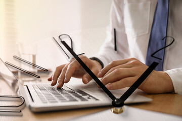 Businessman working on laptop at table, clock, double exposure. Time management