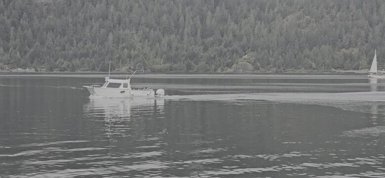 A aerial drone shot of a lone fishing trawler with beautiful forest and coastline in the distance near