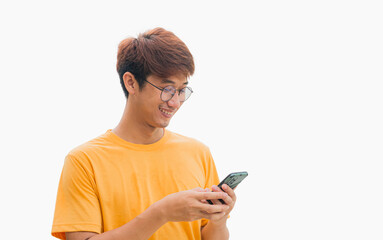 Young Asian man in his 20s wear glasses and wearing a yellow t-shirt is happily playing on a mobile phone isolated on a gray background. Typing and chatting with friends via smartphone. Online social