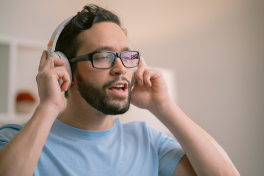 Young man listening to music on headphones and singing at home