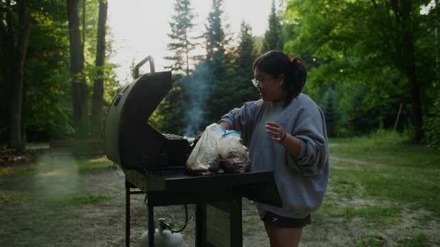 A lady grills kalbi beef in the front yard, backlit by the sun, capturing the rich textures of the meat and the warm glow of sunlight, creating a visually appealing outdoor cooking scene.