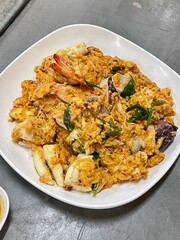 Omelette with shrimp and seafood on rice and sauce on white ceramic plate and spoon and fork.Omelette with shrimp and seafood on rice and sauce on white ceramic plate and spoon and fork.