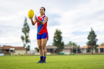 young woman football player in red and blue uniform catching ball on suburban football oval