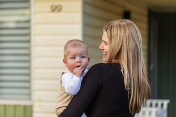 Baby in mums arms looking over his mother's shoulder outside home