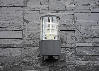 An electric lamp is installed on a black brick wall.