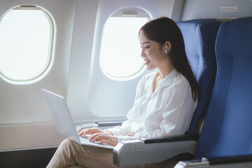 Fototapeta premium A beautiful woman enjoys her airplane journey, sitting comfortably and smiling. Captured in vibrant photography, she epitomizes excitement and happiness, using wireless technology to stay connected du