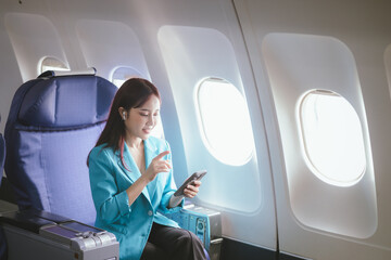 A confident and beautiful young woman enjoys a comfortable flight with a smile on her face while listening to music through her headphones. Sitting by the window, she exudes success and elegance.