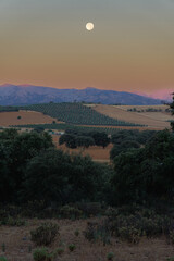 mountain scenery with full moon in the background and colorful sky at dawn