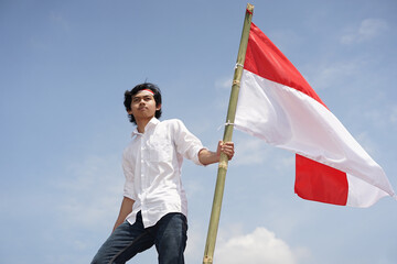 Young Man Holding Indonesian Flag Against Blue Sky