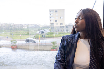 Fototapeta premium A professional woman looking thoughtfully out a window in a modern office setting with an urban landscape.