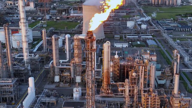 Aerial view of a chemical plant at sunset. Drone shot. Curling fire and cumin smoke filling the sky. Smoking chimneys from the factory. Chimneys of an oil refinery at sunrise pollute the environment