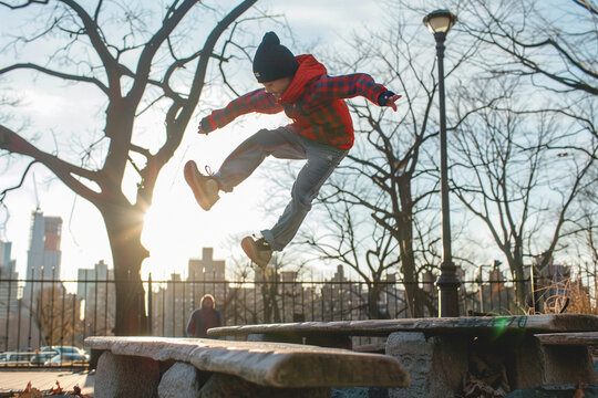 A teenager practicing parkour skills, leaping and running across park benches and sculptures