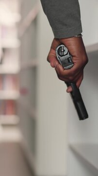 Man with gun prepares attack on public library closeup. African American guy holds handgun walking across literature storage. Criminal actions
