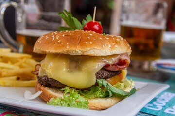 Deliciosa hamburguesa con queso, tocino, vegetales y papas fritas en un plato.