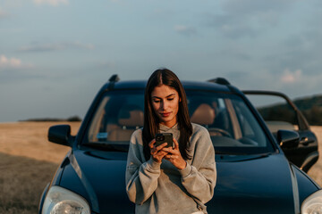 Young beautiful woman traveling by car in the mountains using smartphone at sunset
