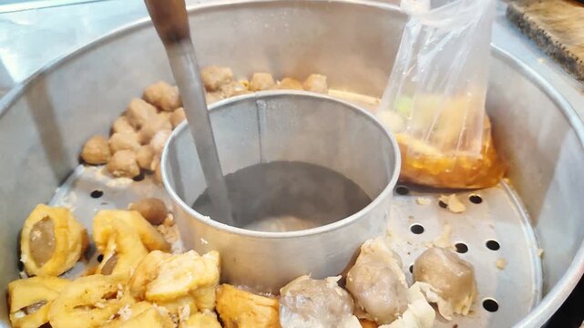 A seller is wrapping bakwan kawi. Bakwan kawi is traditional food from Indonesia. This containing tofu, dumpling and meatball.