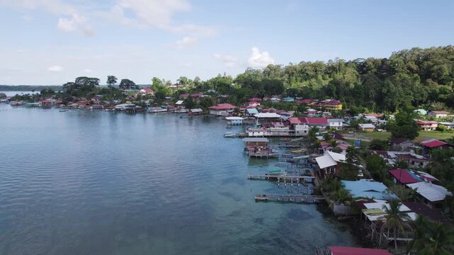 Aerial view of Bastimentos Island's picturesque coastline in Panama, featuring vibrant homes and lush greenery by the water. dolly forward