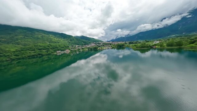Serene aerial view of Lago di Levico with lush green hills and town reflections on a cloudy day