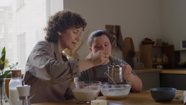 Girl with Down syndrome sifting flour into bowl with help of female teacher during baking lesson