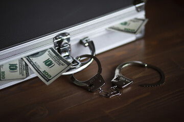 Handcuffs and Cash with Silver Briefcase on Wooden Surface: Crime, Finance, and Security Concept