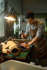 Craftsman wearing a brown apron using mallet to punching holes on piece of leather