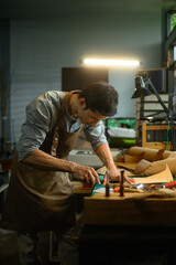 Concentrated artisan carefully using a sharp knife to shape the leather on cutting mat in his workshop. Handicraft business concept