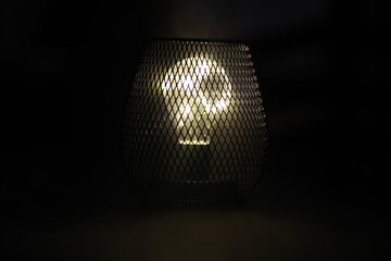 Vintage Abstract Mesh Cage Light Bulb Emitting Warm Glow in Dark Background