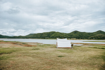 White camping picnic tent campground in outdoor park lake with mountains and blue sky with white clouds in the background. Adventure travel and vacation concept
