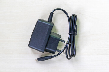 A black plastic mobile charger lies on wooden surface. Top view.