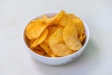 Bowl of crispy potato chips or crisps on light wooden background. Delicious Lays Spanish tomato tango potato chips.
